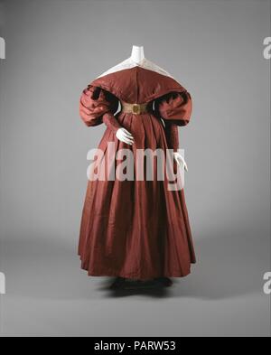 Walking ensemble. Culture: American. Date: ca. 1835.  The 1830s silhouette was created by a corseted, raised waistline; here a bell-shaped skirt reveals the lower ankle.  By the late 1830s, the gigot sleeve was collapsing at the sleeve cap, but in this case, its detachable pelerine, or capelet, sustained the broad triangulated shoulder line of the period. The similarities between men's and women's fashion extended to footwear: women could wear flat slippers or tiny booties not so different from the boots and walking shoes of men. Museum: Metropolitan Museum of Art, New York, USA. Stock Photo