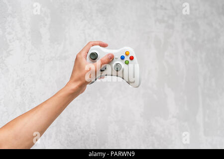 Hand holding gamepad on grey concrete background. Man with controller playing video game at home. Leisure and entertainment. Video game console contro Stock Photo