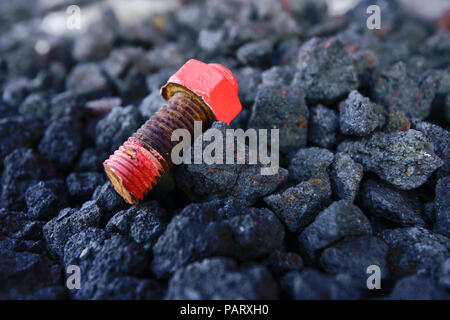 Old rusty red screw laying on black coal Stock Photo