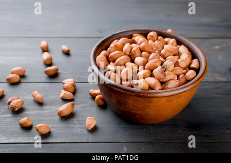 Raw peeled peanuts in a brown ceramic bowl on old dark wooden background, selective focus Stock Photo