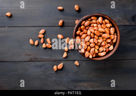 Raw peeled peanuts in a brown ceramic bowl on old dark wooden background, selective focus Stock Photo