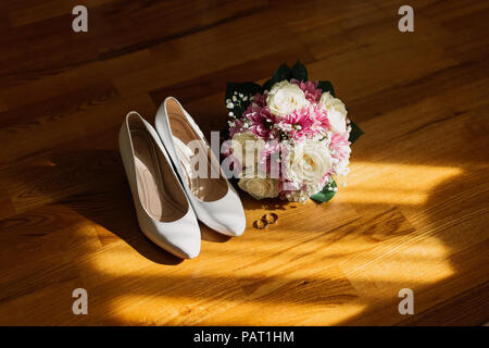 Brides wedding shoes with a bouquet with roses and other flowers on tha arm chair. Stock Photo