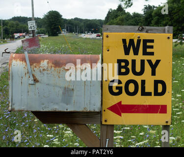 A beat up bright yellow We Buy Gold sign with a red arrow next to a rusty old mail box on a side road in upstate NY, USA Stock Photo