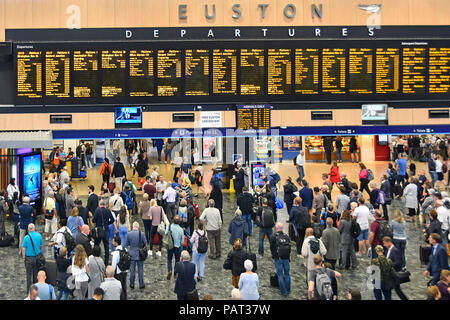 View from above looking down at interior of Euston railway station concourse with passengers viewing train departures travel information London UK Stock Photo