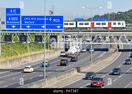 View from above looking down on traffic M25 motorway gantry road sign junction 28 Brentwood Essex Greater Anglia train on railway bridge England UK Stock Photo