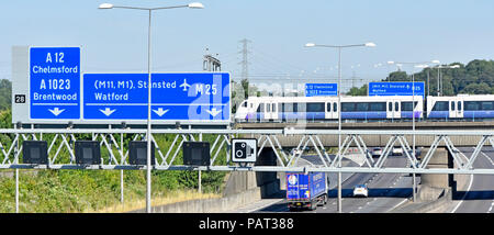 M25 motorway gantry road sign junction 28 Brentwood Essex Elizabeth line new Crossrail Bombardier Aventra train to London on railway bridge England UK Stock Photo