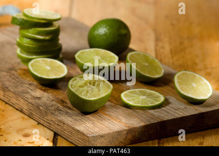 Whole sliced and halved limes on wood chopping board Stock Photo
