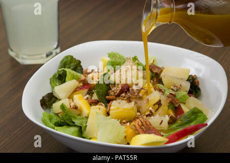 Apple, pineapple, nuts and lettuce salad with dressing falling on it and fresh lemonade on a wood table Stock Photo