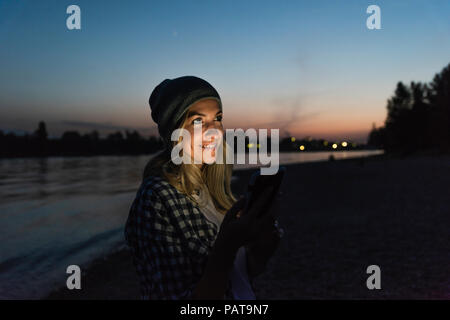 Young woman using smartphone on riverside in the evening Stock Photo