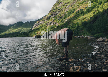 Norway, Lofoten, Moskenesoy, Young man washing his face in Agvatnet lake Stock Photo