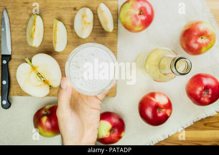 Flat lay with glass of sparkling cidre drink on rustic wooden table. Point of view of hand holding glass of home made cider and locally grown organic  Stock Photo