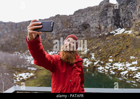 Iceland, smiling bearded man using smartphone, selfie Stock Photo