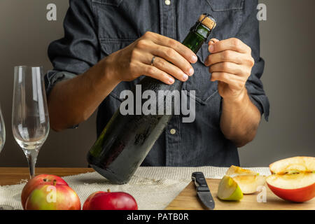 Male hands opening bottle of premium cidre. Uncorking beautiful ice cold bottle of apple wine, with ripe apples in background Stock Photo