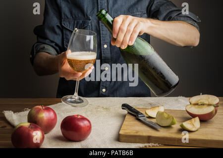 Male hands pouring premium cidre in wine glass above rustic wood table. Tasting vintage apple cider out of ice cold bottle Stock Photo