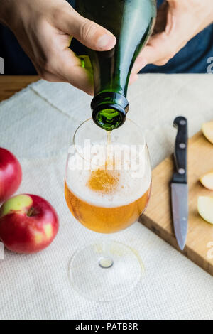 Close-up image of man pouring premium cidre in glass. Top view of male hands pouring vintage apple wine into beautiful glass in rustic table backgroun Stock Photo
