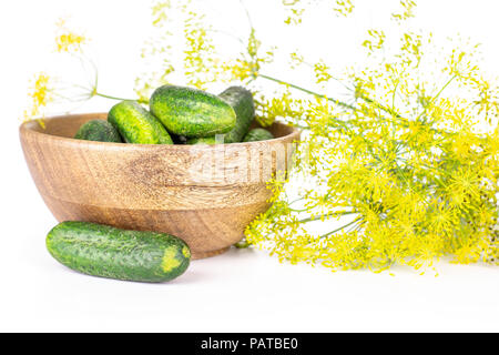 Lot of whole fresh yellow dill flowers and wooden bowl full of cucumbers isolated on white Stock Photo