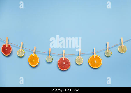 Slices of orange, grapefruit, lemon and lime hanging on a rope, attached with wooden pins. Light blue background, space for text. Stock Photo
