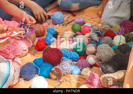 Group of women crocheting or knitting sitting grouped around a pile of colorful wool and yarns on the ground Stock Photo
