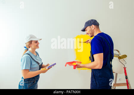 Couple decorating room using paint rollers and paintbrush on wall Stock Photo