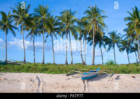 Small striped fishing boat docked on a white sand beach below palm trees - Nacpan, El Nido - Palawan, Philippines Stock Photo