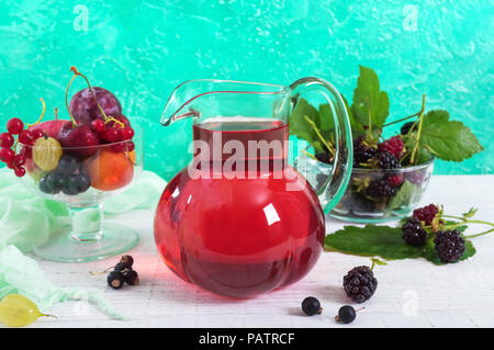 Berry compote. Fruit vitamin drink in a glass jug and ripe fresh berries on a bright background. Stock Photo