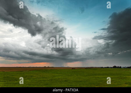 Evening storm. Dramatic clouds and sky over green fields and power plant Stock Photo