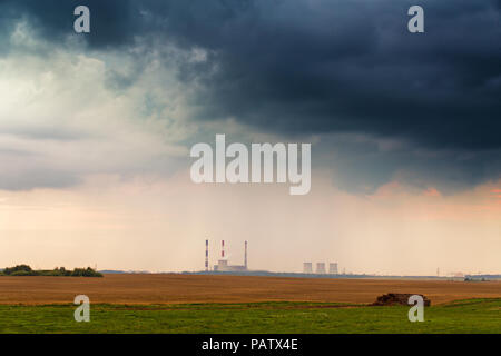 Panoramic view of power plant under stormy dramatic clouds. Power station at sunset time with golden wheat field Stock Photo