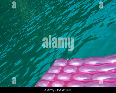 Detail of a pink  inflatable pad (mattress) with water drops on the surface floats  in blue green  transparent sea water Stock Photo