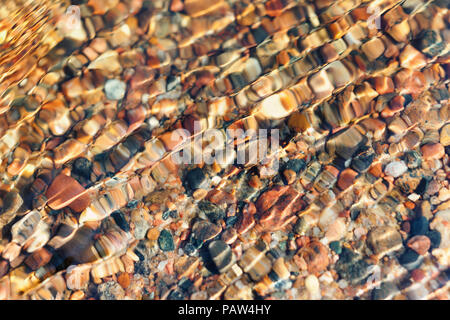 Rocks on the sandy bottom of the sea ripples through small waves on a sunny day Stock Photo