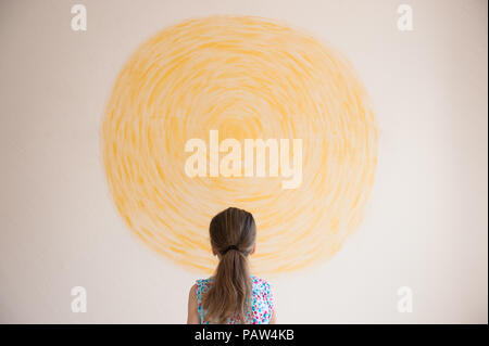 little caucasian girl looking at yellow sun painted on wall indoors Stock Photo