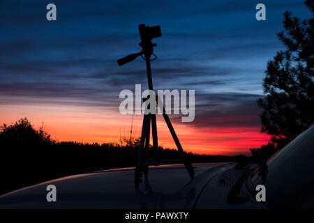 Closeup of mirrorless camera and tripod on the hood of a car during a colorful Lake Tahoe forest sunset. Stock Photo