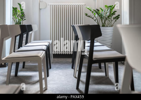 Rows of black and white chairs in the conference room with white walls and a gray floor. There are green plants in the pots behind them. Closeup horiz Stock Photo