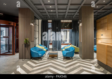Beautiful hallway with luminous lamps in the hotel with dark ceiling and patterned tiled floor. There is a glass entrance door, multicolored armchairs Stock Photo