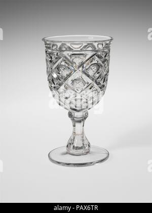 Goblet. Culture: American. Dimensions: H. 6 1/4 in. (15.9 cm); Diam. 3 5/16 in. (8.4 cm). Date: 1850-60.  With the development of new formulas and techniques, glass-pressing technology had improved markedly by the late 1840s. By this time, pressed tablewares were being produced in large matching sets and innumerable forms. During the mid-1850s, colorless glass and simple geometric patterns dominated. Catering to the demand for moderately-priced dining wares, the glass industry in the United States expanded widely, and numerous factories supplied less expensive pressed glassware to the growing  Stock Photo