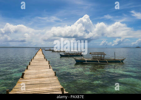Island 'walkway' jutting out into a beautiful cloudy sea, with fishing boats docked nearby - Siargao, Philippines Stock Photo