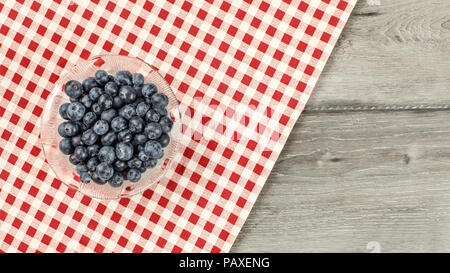 Tabletop view -  small bowl of blueberries, with red chequered tablecloth on gray wood desk Stock Photo