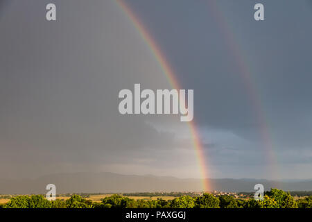 Majestic nature concept. Rainbow over a quaint village and meadows, after the rain, copy space, wallpaper. Stock Photo