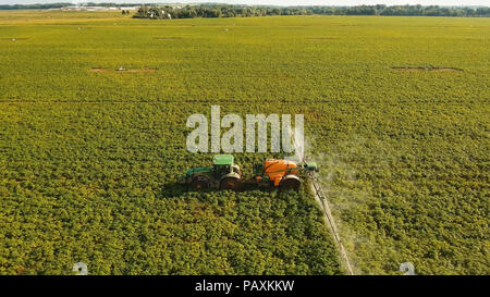 Aerial view tractor spraying the chemicals on the large green field. Spraying the herbicides on the farm land. Treatment of crops against weeds. Stock Photo