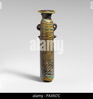 Glass alabastron (perfume bottle). Culture: Greek, Eastern Mediterranean. Dimensions: H. 5 1/2 in (14 cm); Diameter: 2 5/8 in (6.7 cm). Date: 5th century B.C..  Opaque dark red brown, with handles in same color; trails in opaque yellow and opaque turquoise blue.  Broad slightly uneven horizontal rim-disk; cylindrical neck; rounded shoulder; straight-sided cylindrical body with slight upward taper; convex bottom; two vertical ring handles with knobbed tails, applied over trail decoration.  Intermingled yellow and turquoise blue trails attached at edge of rim-disk; a yellow trail applied to bott Stock Photo