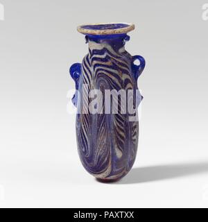 Glass alabastron (perfume bottle). Culture: Greek, Eastern Mediterranean. Dimensions: H.: 2 1/2 in. (6.4 cm). Date: late 6th-5th century B.C..  Translucent cobalt blue, with handles in same color; trails in opaque white.  Slightly concave horizontal rim-disk, with projecting rough edge to mouth; cylindrical neck; narrow rounded shoulder; slightly convex sides to cylindrical body, tapering upwards; convex bottom; two vertical ring handles with knobbed tails, applied over trail decoration; one larger and higher than the other.  A trail attached at edge of rim-disk; another trail applied on neck  Stock Photo