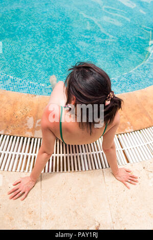 Young woman with red sunburned skin on her shoulder sitting near swimming pool. Sunburn concept. Stock Photo