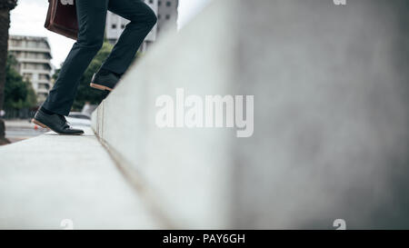 Low angle view of legs of man climbing up the steps outdoors. Legs of man wearing formal clothes and shoes carrying an office bag walking up the stair Stock Photo