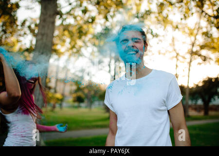 Woman throwing powder paint her boyfriend. Couple playing with colored powder in the park. Stock Photo