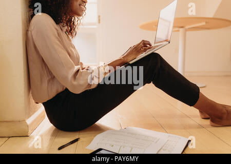 Side view of a woman entrepreneur in formal attire working on laptop computer sitting at home. Businesswoman sitting on floor at home working on lapto Stock Photo
