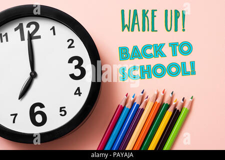 closeup of a clock, some pencil crayon of different colors and the text wake up back to school on a pink background Stock Photo