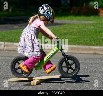 A little girl (3 yr old) riding her balance bike across a jump made of bits of wood Stock Photo