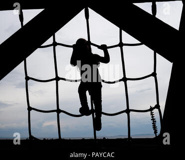 A silhouette of a three year old girl climbing a rope ladder Stock Photo