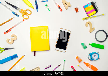 mobile phone and yellow notebook in the desk. white background. concept of education. back to school. creative mess on the desktop. desk. stationery.  Stock Photo