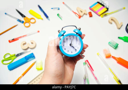 back to school. blue alarm clock on the school desk in the hands of a student. stationery. accessories. White background. stickers, colored pens, penc Stock Photo