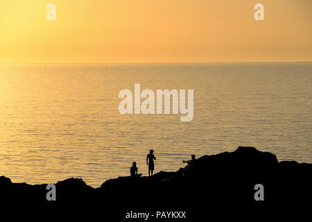 Friends watching the sun go down on the coast at Porth Beach, Newquay Stock Photo